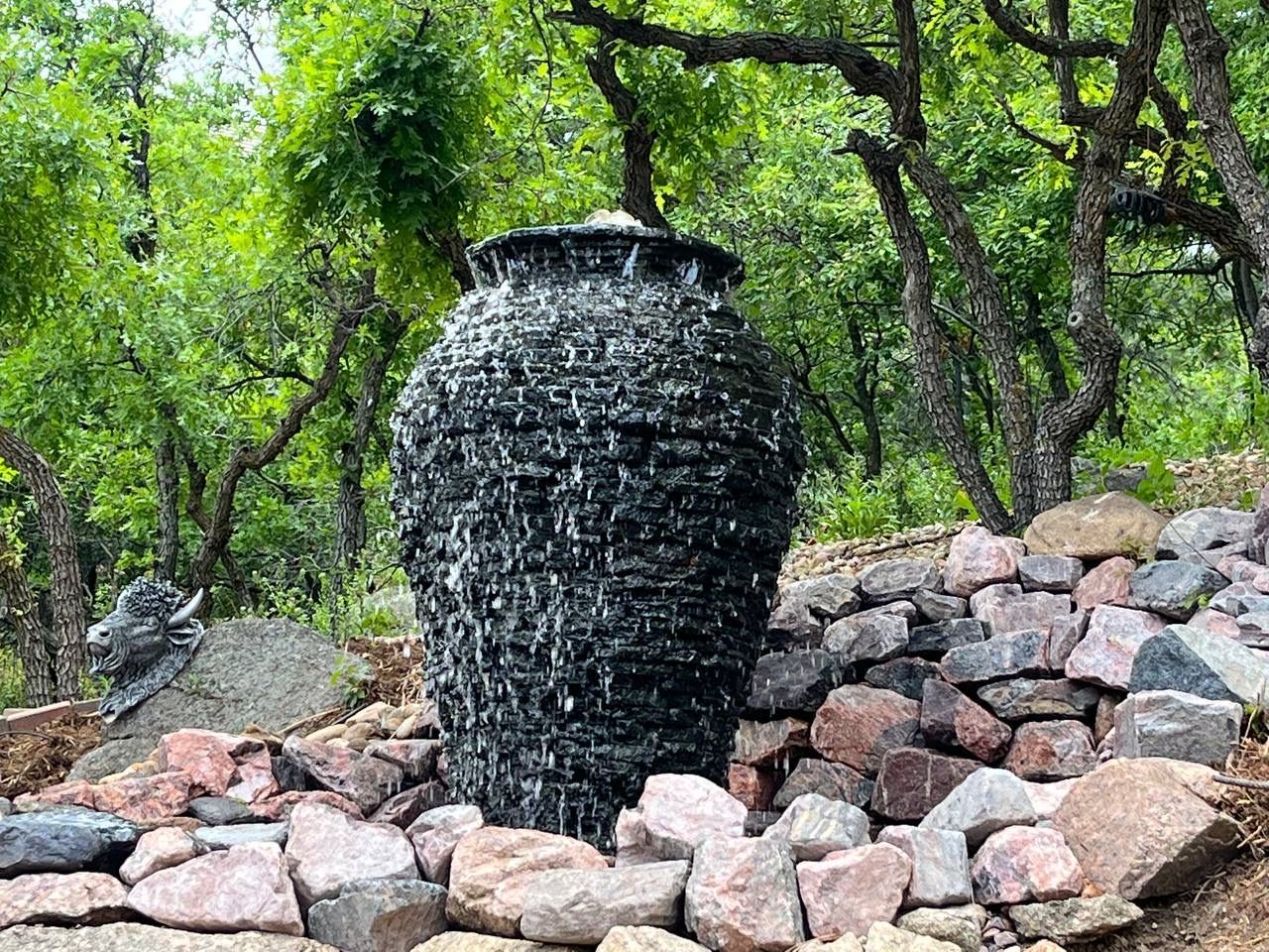 A large vase filled with water is surrounded by rocks in the middle of a forest.