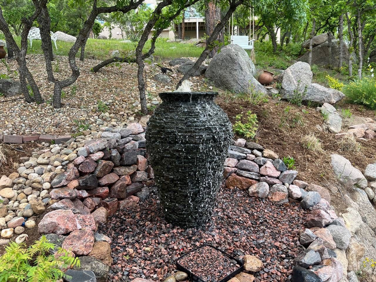 A fountain is surrounded by rocks and trees in a garden.