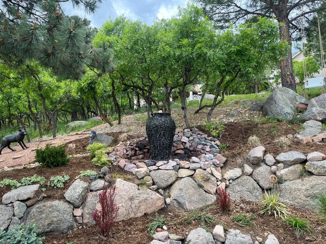 A dog is standing next to a fountain in a rock garden.