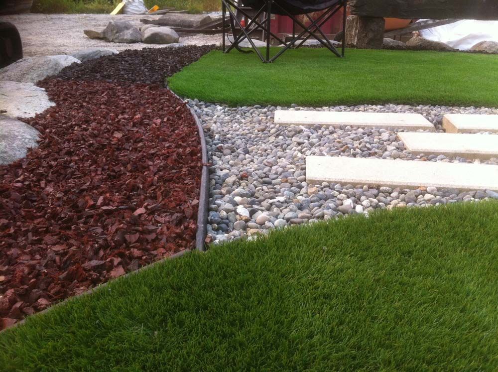 Landscaped yard with artificial turf, bark mulch, pebbles, and stepping stones.