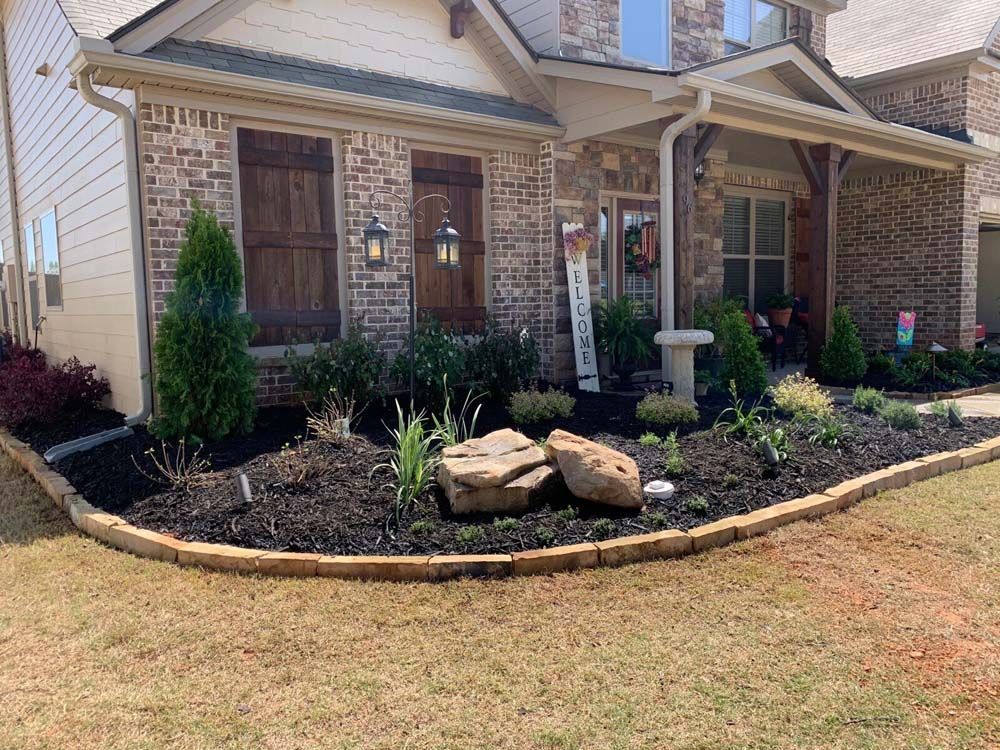 Landscaped front yard with brick house, mulch, plants, and decorative rocks.