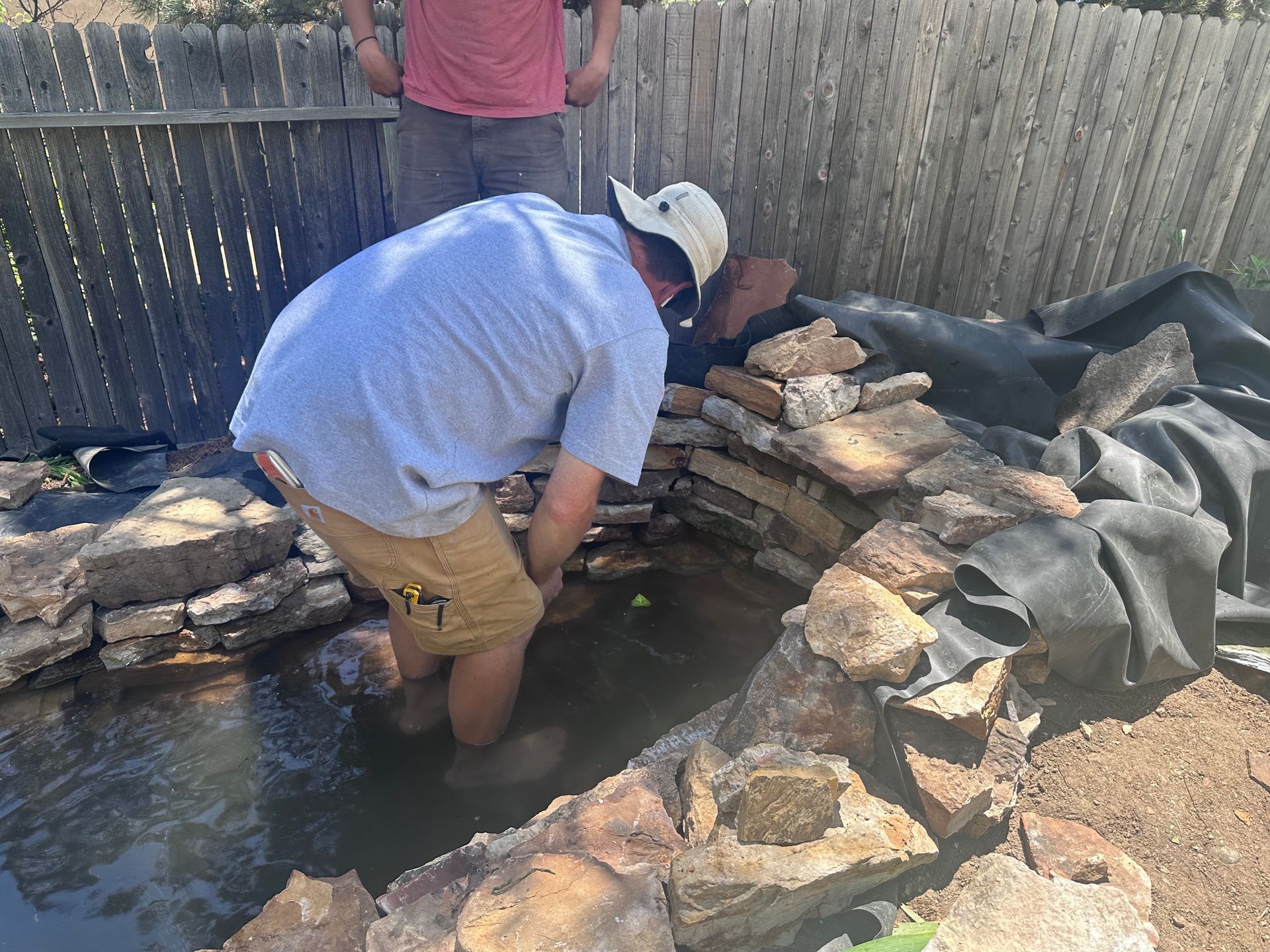 A man wearing a hat is kneeling in a pond