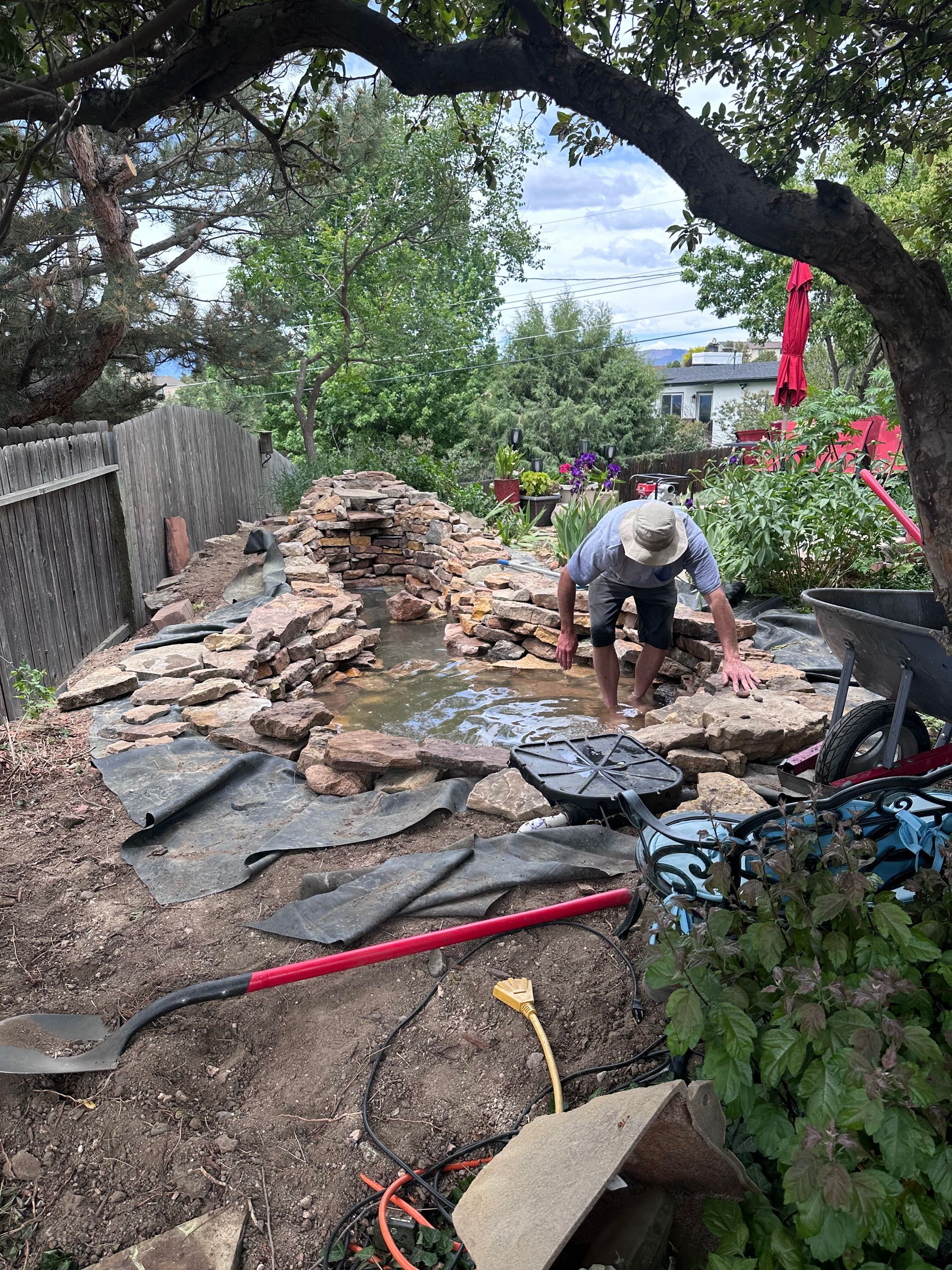 A man is working on a pond in a backyard.