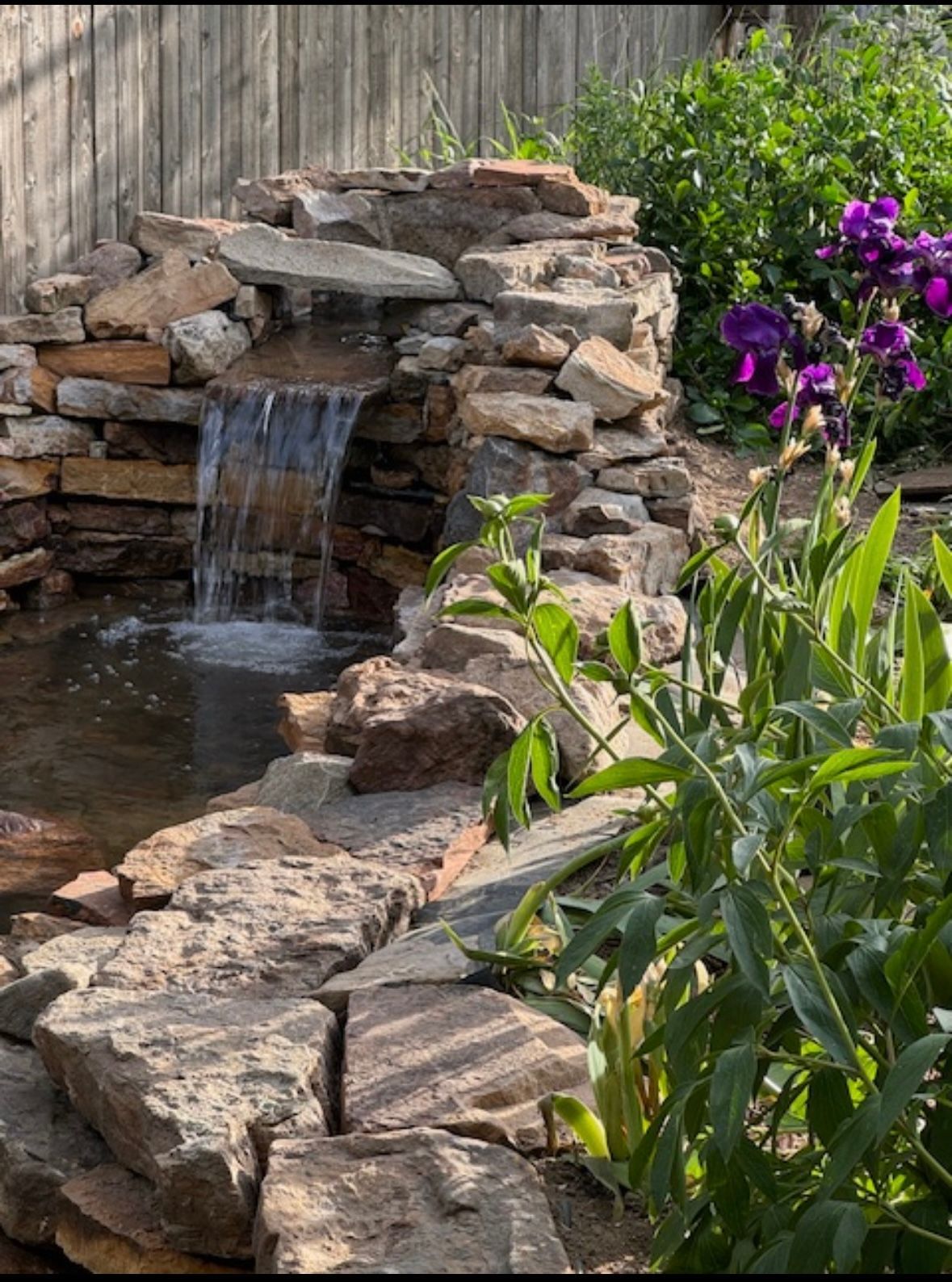 A waterfall is surrounded by rocks and flowers in a garden.