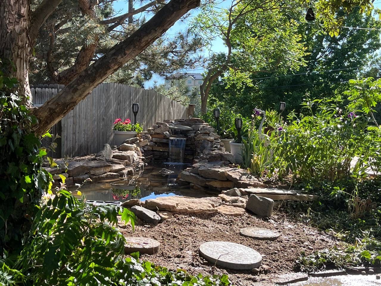 A waterfall in a garden with a wooden fence in the background