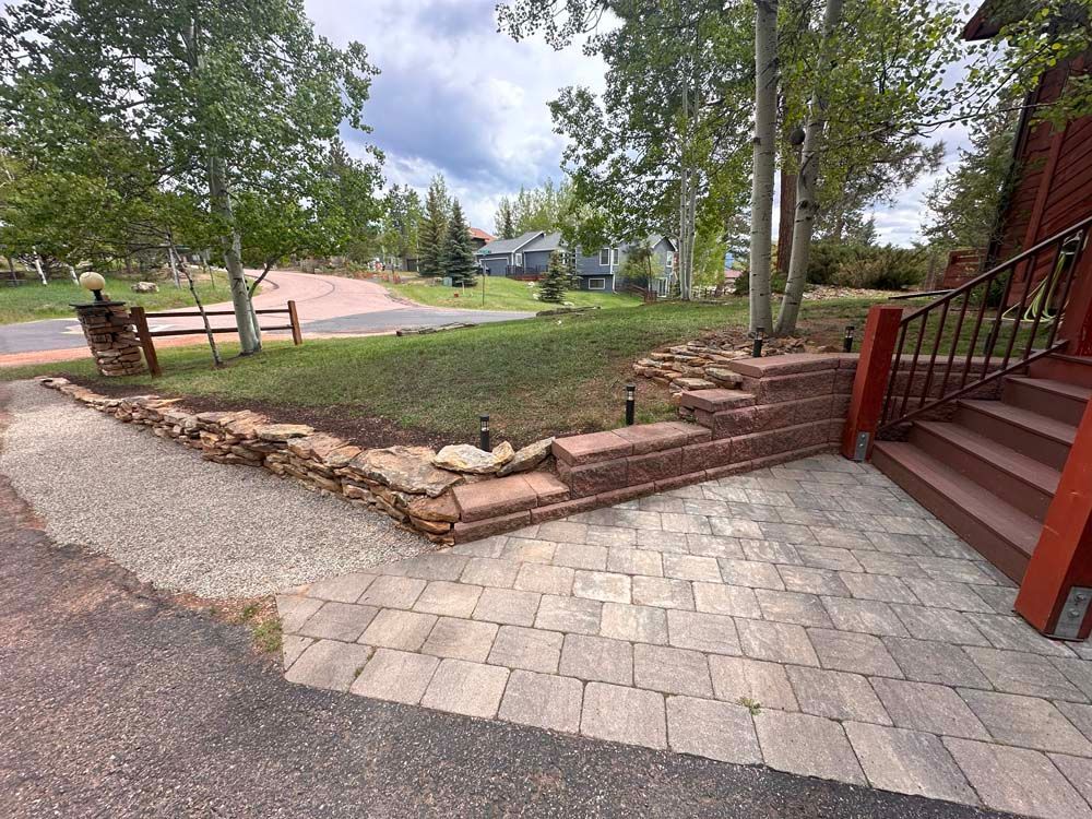 A brick and stone pathway leading to a house with steps. Trees and grass surround it. Cloudy sky.