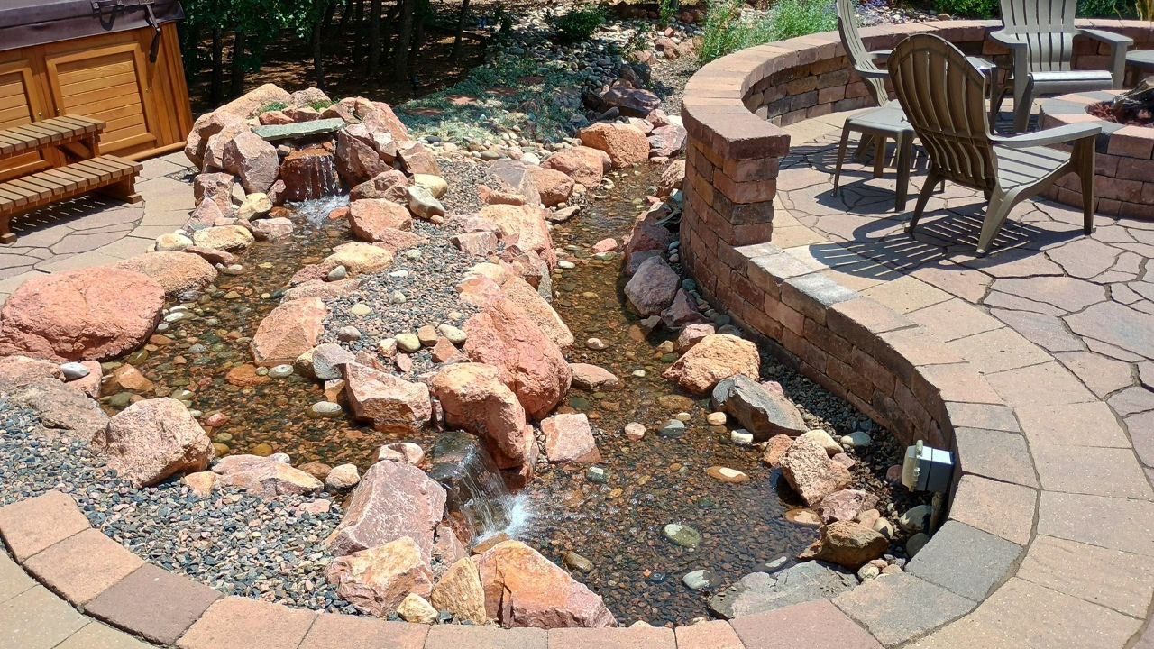 A pond surrounded by rocks and bricks with a hot tub in the background