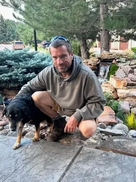 A man is kneeling down next to a dog in a garden.