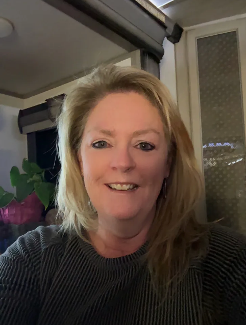 A woman in a gray sweater is smiling for the camera.