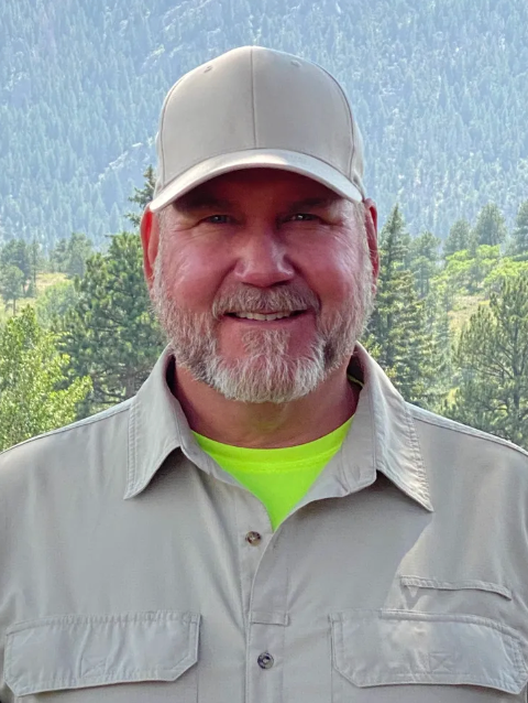 A man with a beard is wearing a hat and a yellow shirt.
