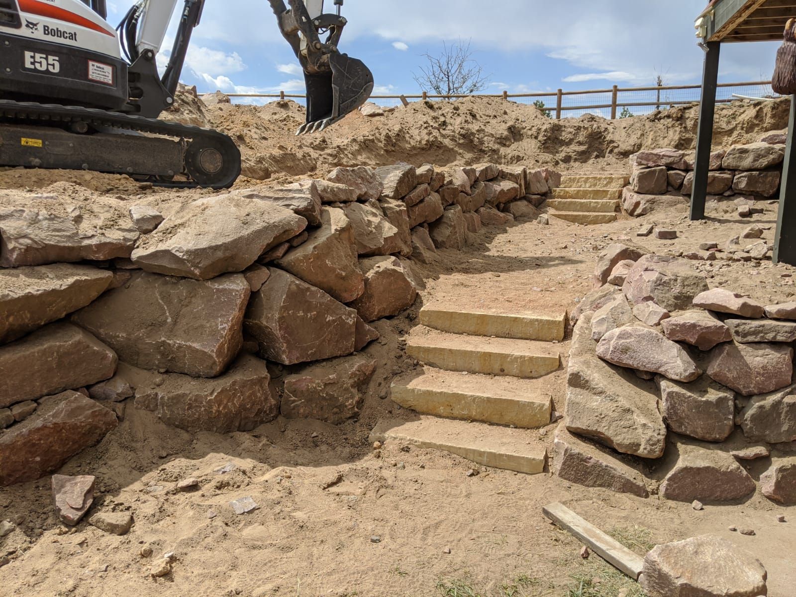 A bobcat excavator is working on a rock wall