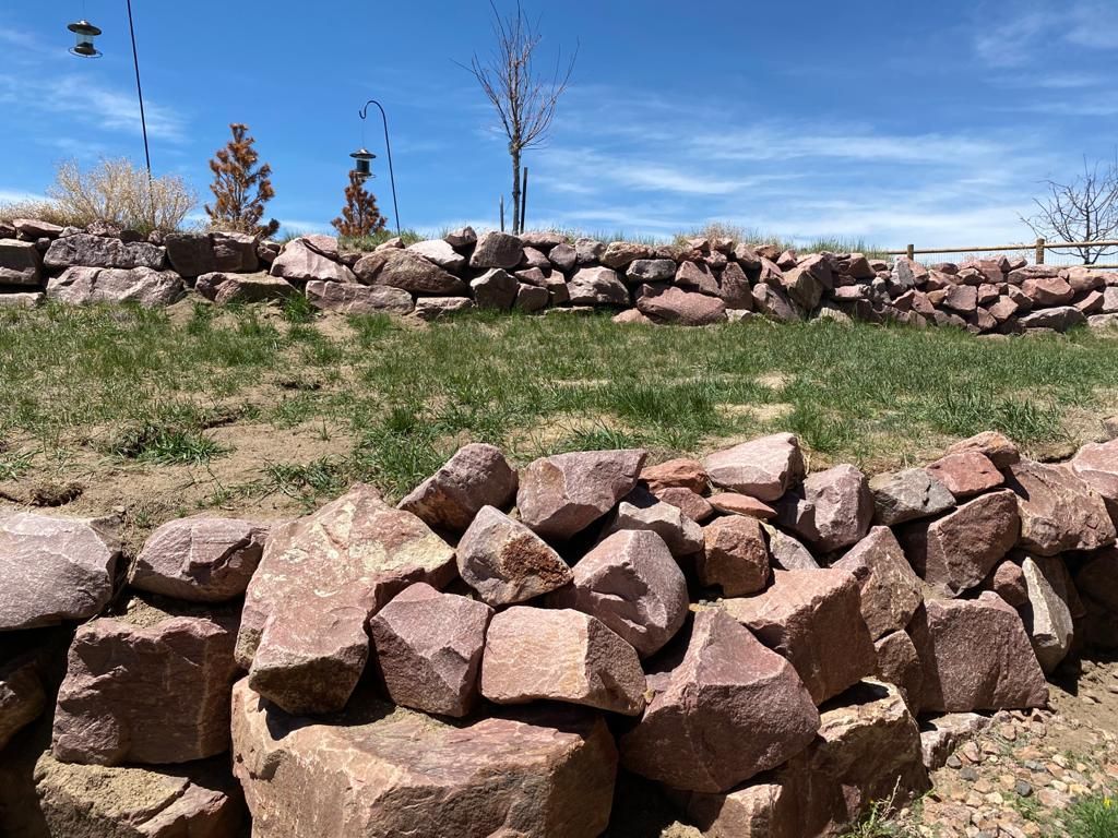 A pile of rocks in a field with a fence in the background