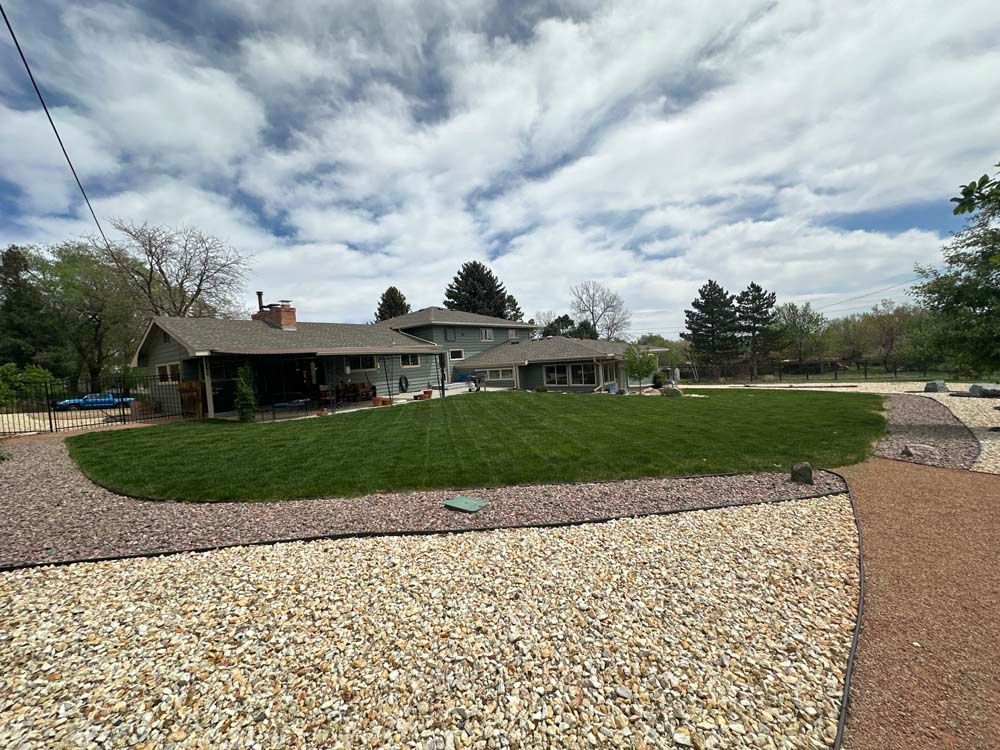 Large house with green lawn, gravel pathways, and cloudy sky.