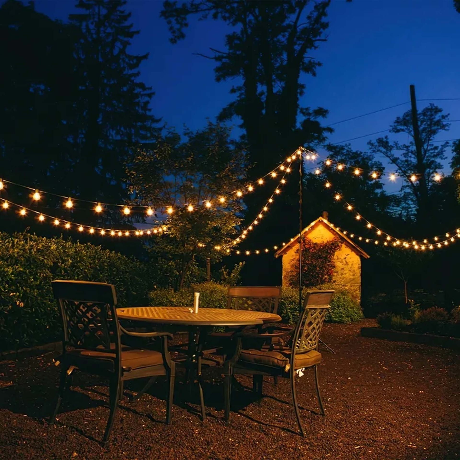 Patio at night with string lights over a table and chairs, small shed in the background.
