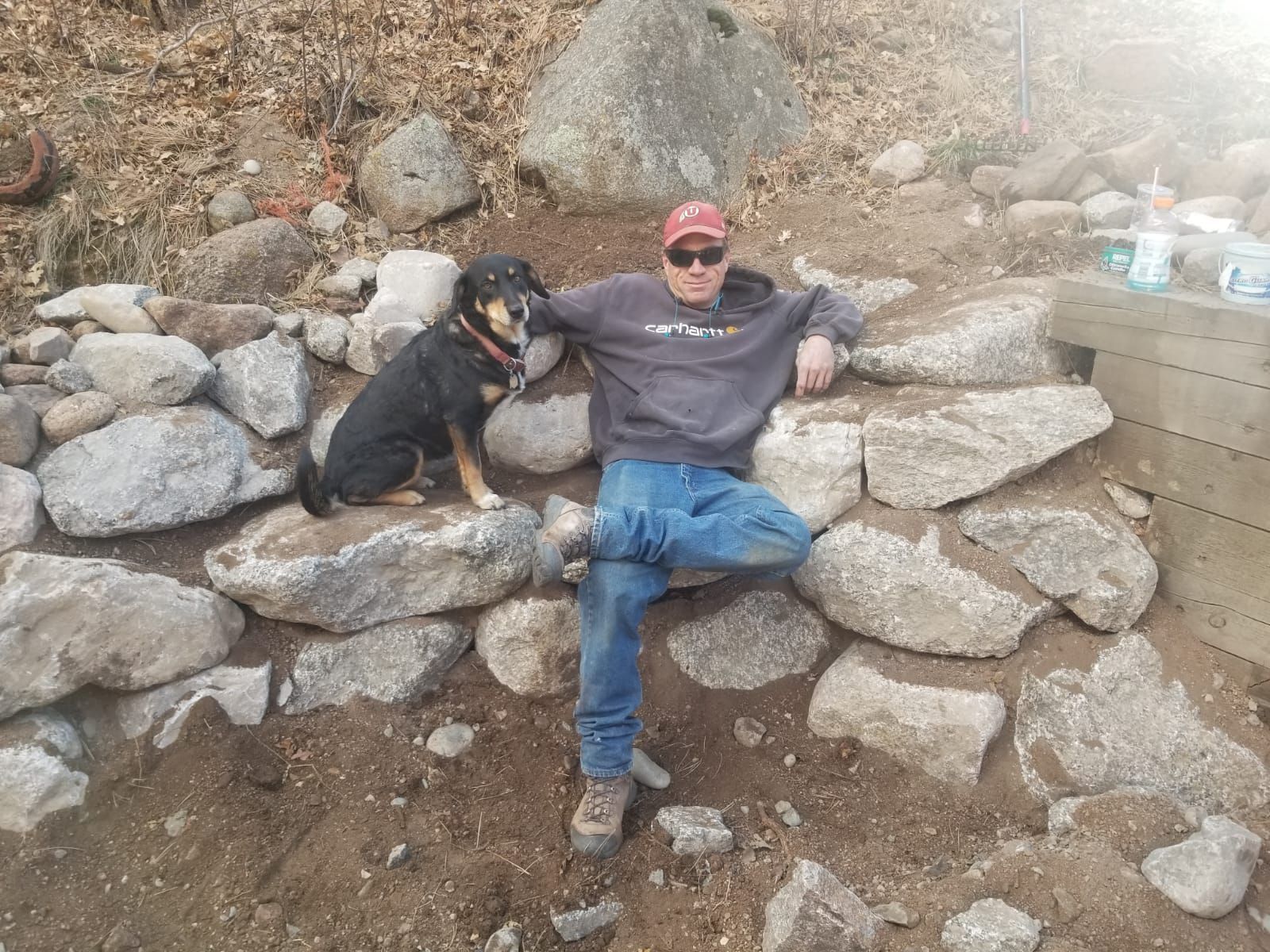 A man and a dog are sitting on a rock wall