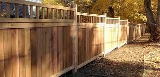 A wooden fence surrounds a yard with trees in the background.