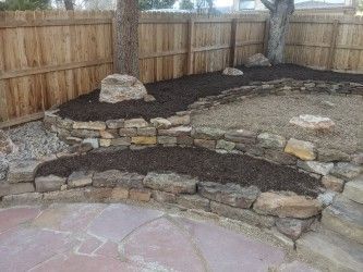 A wooden fence surrounds a stone wall in a backyard.