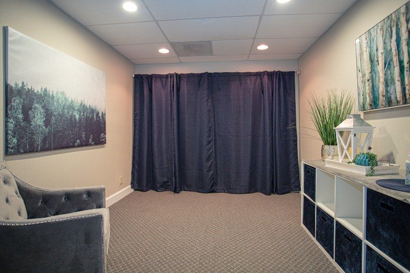 A room with blue curtains , a chair , a shelf and a painting on the wall.