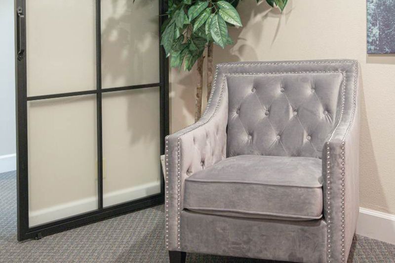 A gray chair is sitting in a room next to a window and a plant.