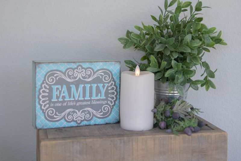 A sign that says `` family '' is sitting on a wooden table next to a candle and a plant.