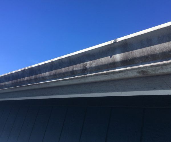 Gray gutter against a blue sky, showing discoloration.