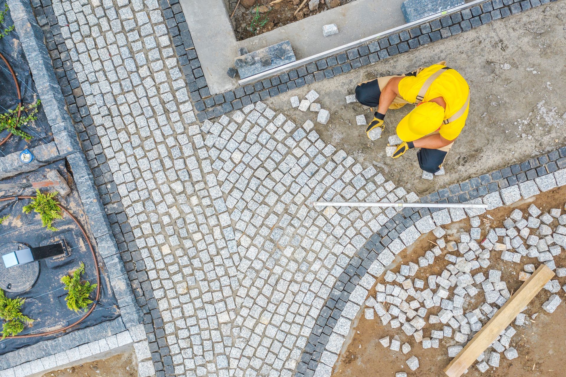 An aerial view of a man laying bricks on a sidewalk.