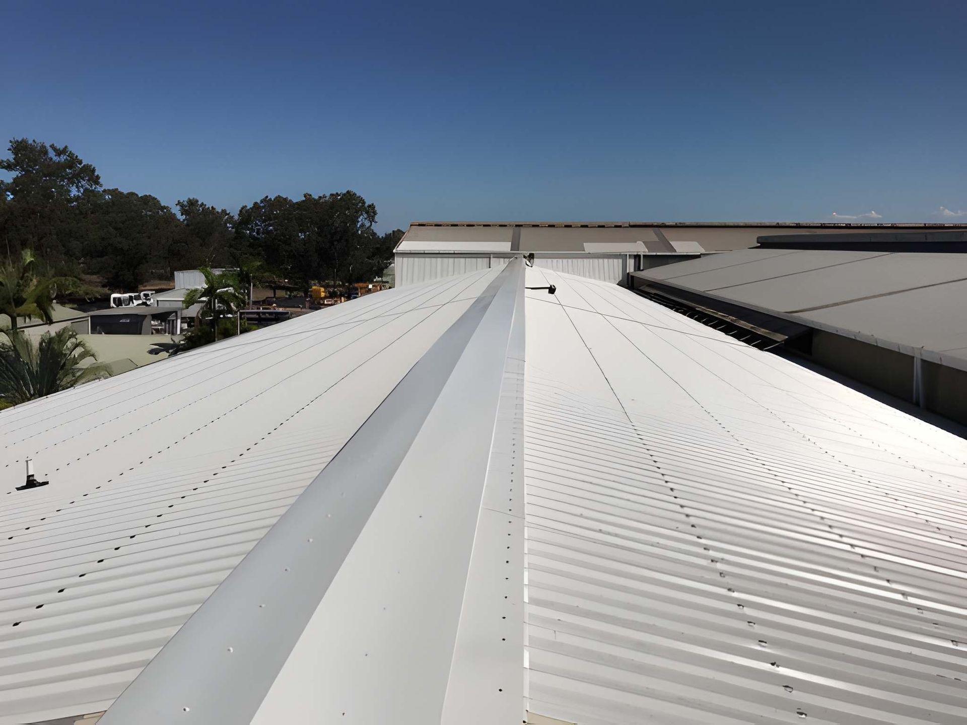 View of a white metal roof with a central ridge. Clear blue sky 