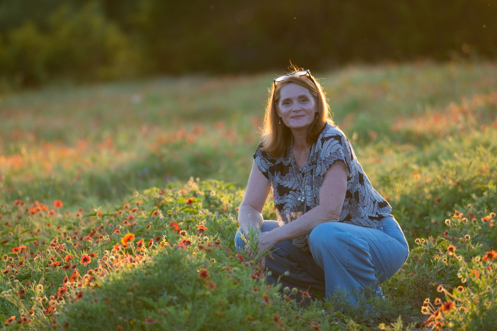 Woman crouching in a field of wildflowers, smiling. Golden sunlight.