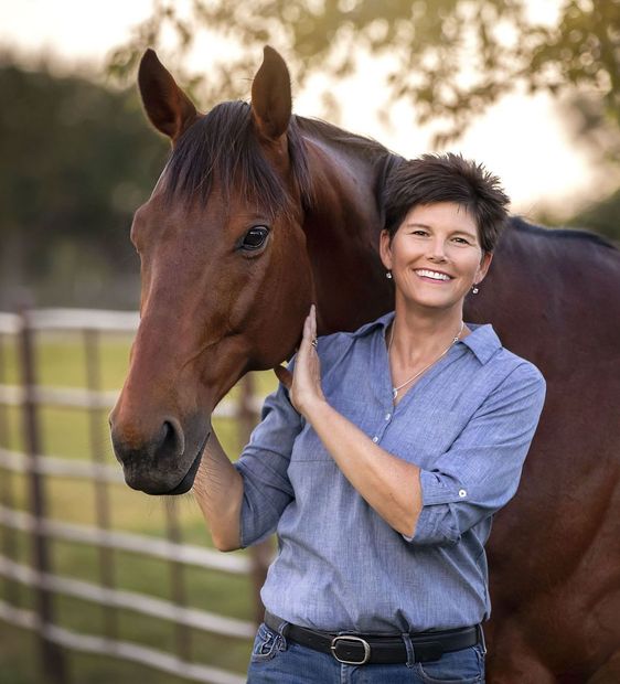 Kathy Taylor in a blue shirt is standing next to a brown horse