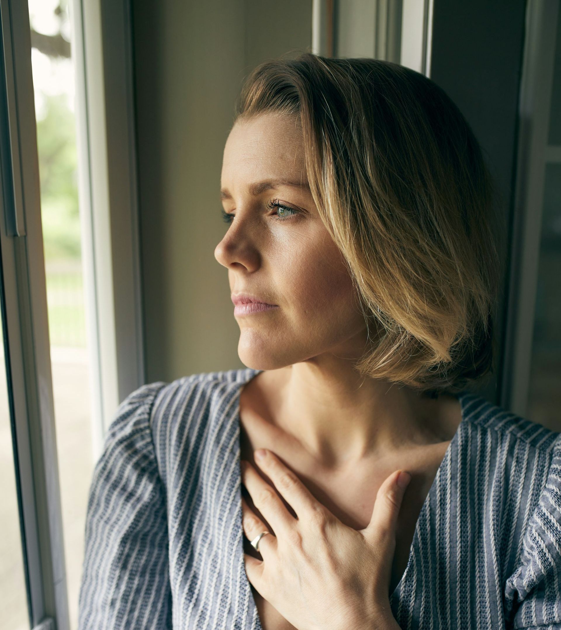 A woman in a striped shirt is looking out a window.