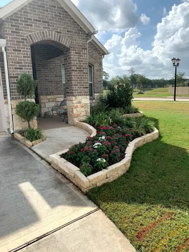 Brick home with a landscaped flower bed, sidewalk, and green lawn on a sunny day.