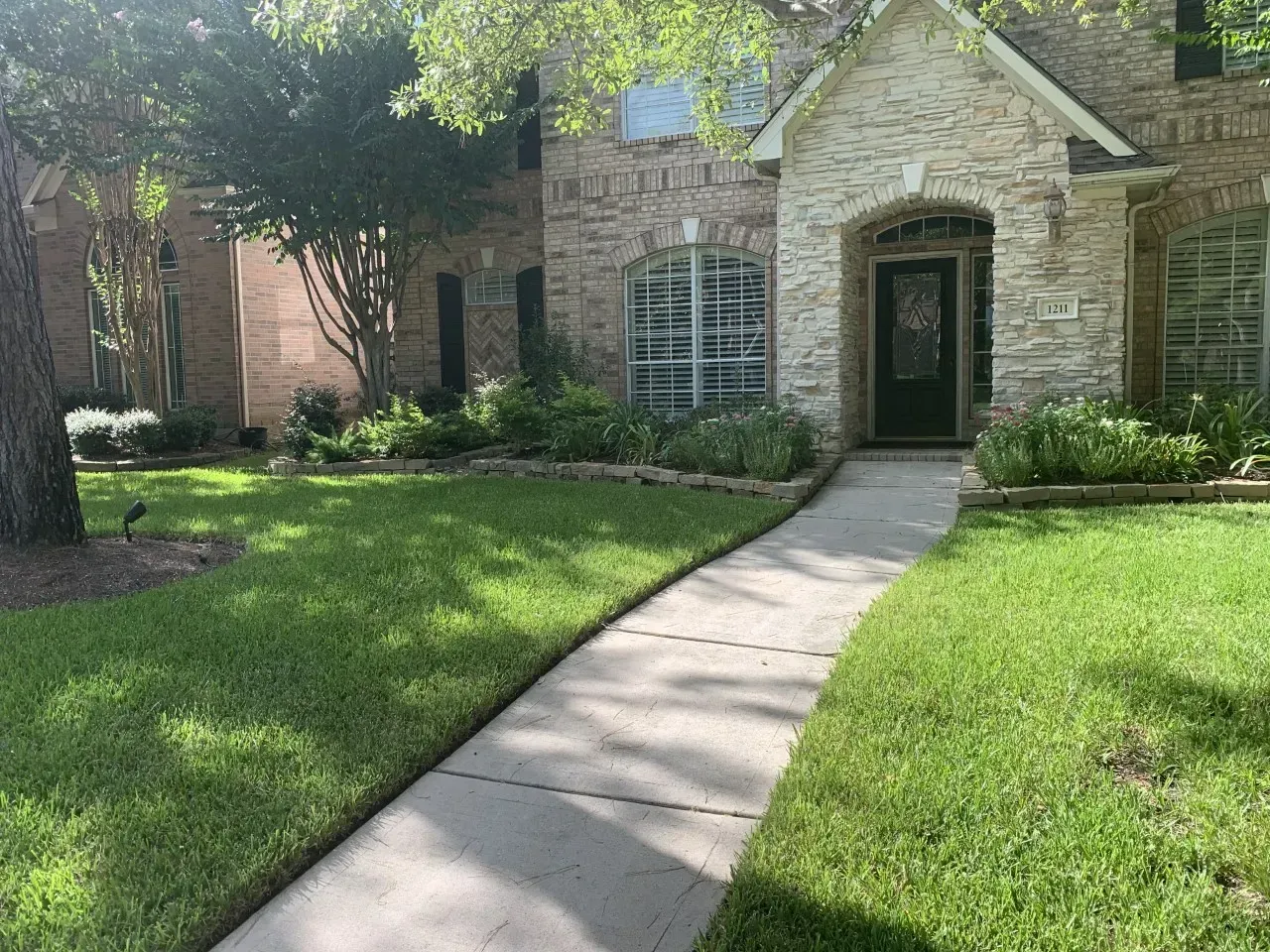 A two-story brick house with a curved walkway, green lawn, and shrubbery.
