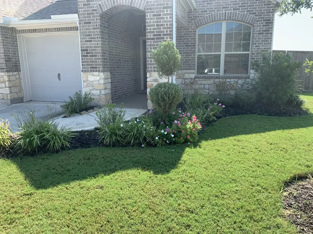 A two-story brick house with a curved walkway, green lawn, and shrubbery.
