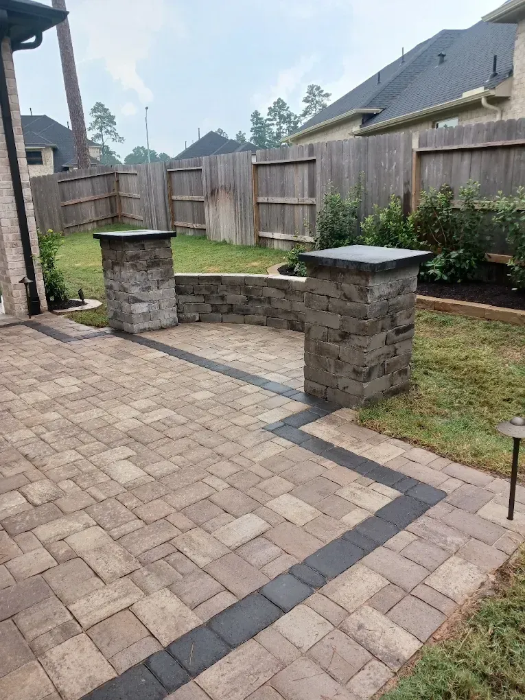 Brick patio with stone pillars and a low wall, leading to a grassy backyard with a wooden fence.