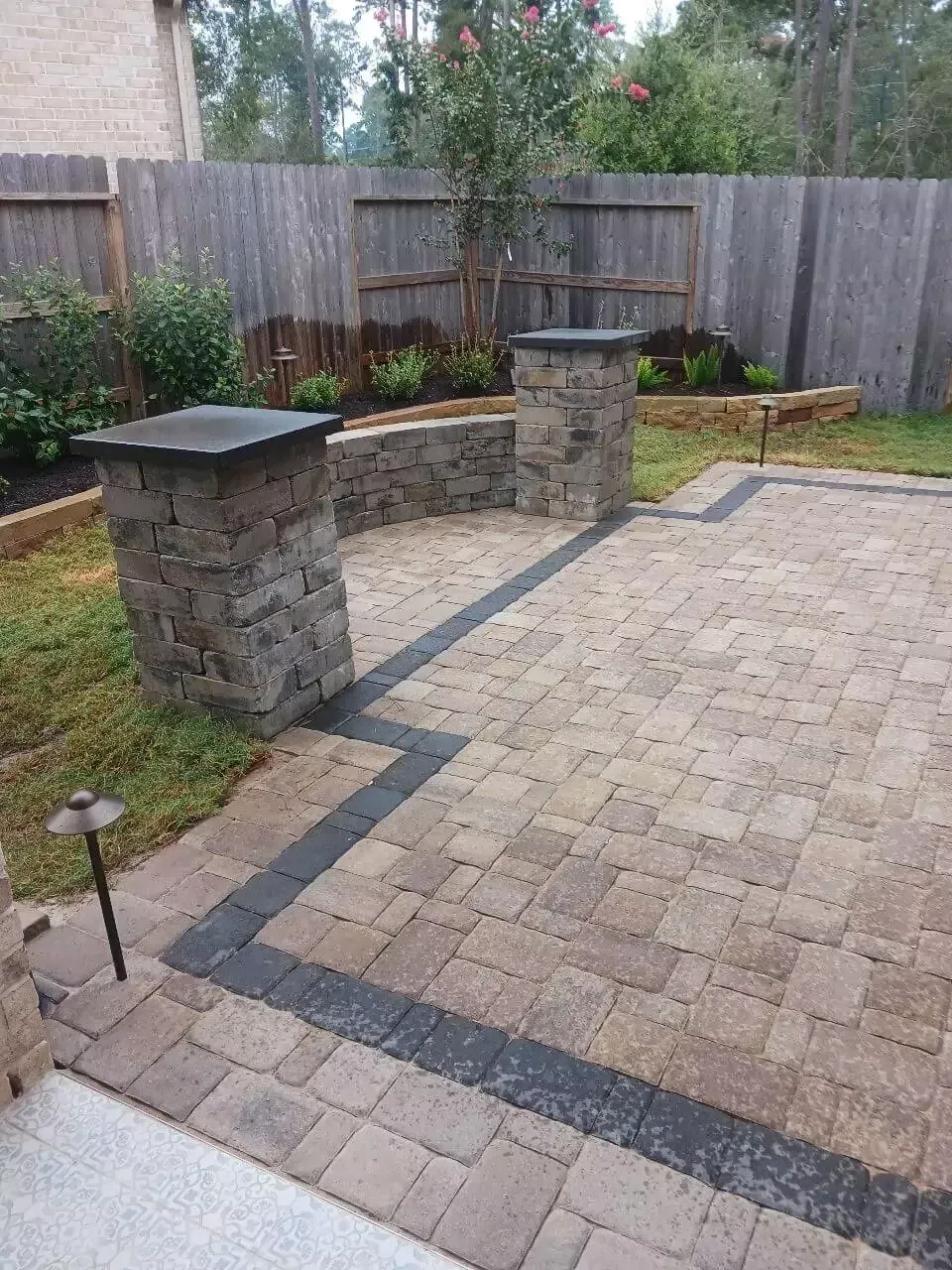 Brick patio with stone pillars and a small garden in a backyard.