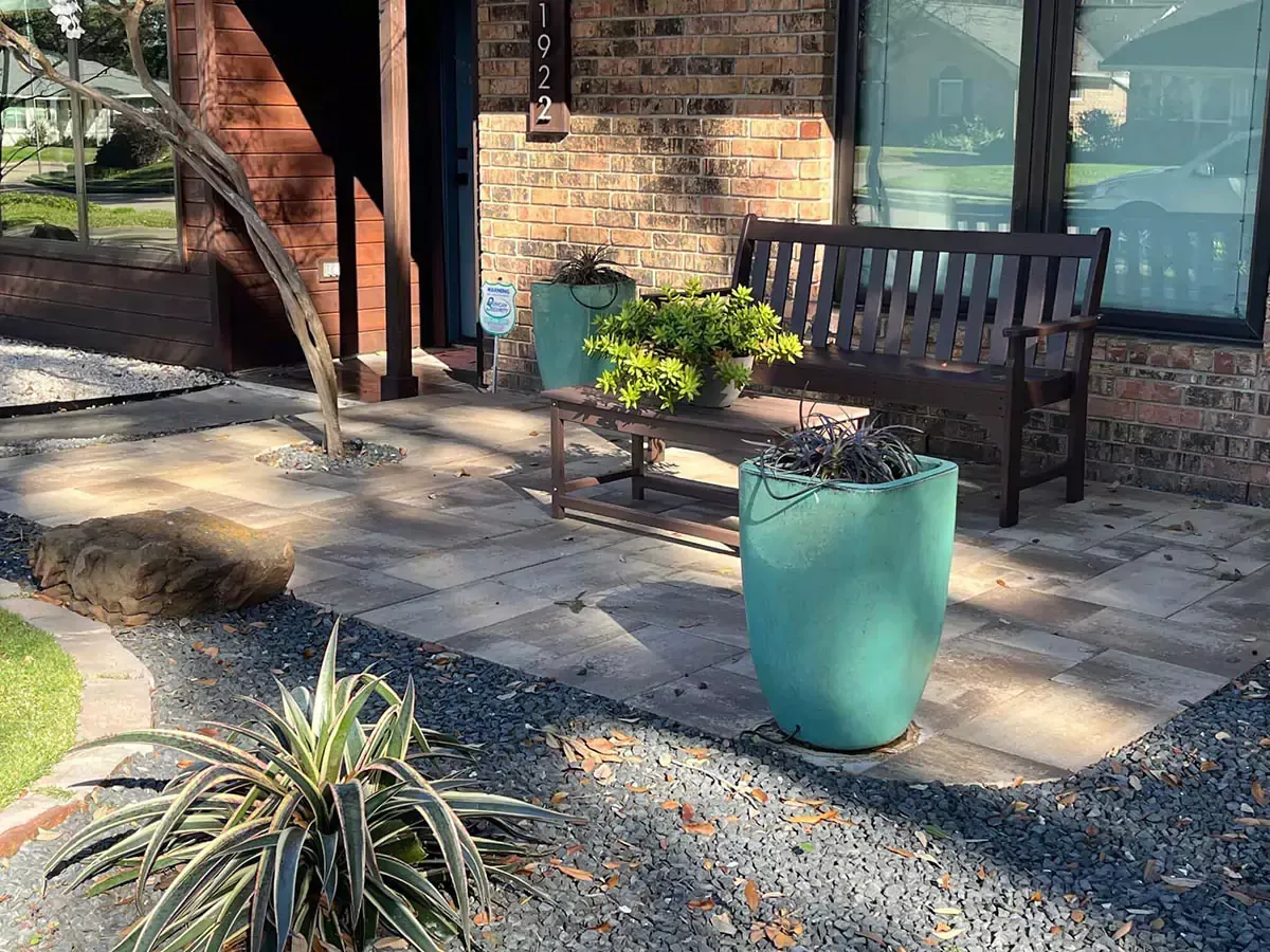Entrance patio with brick facade, wooden bench, teal planters, and gray pavers.