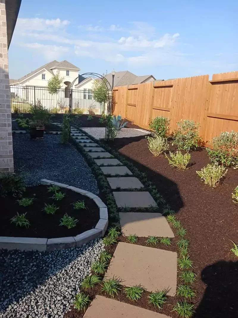 Stone path winds through landscaped backyard with wooden fence.