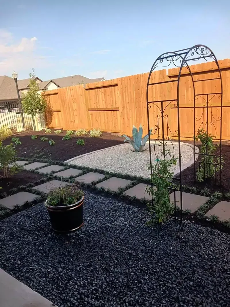 Backyard garden with stone path, black mulch, and wooden fence.