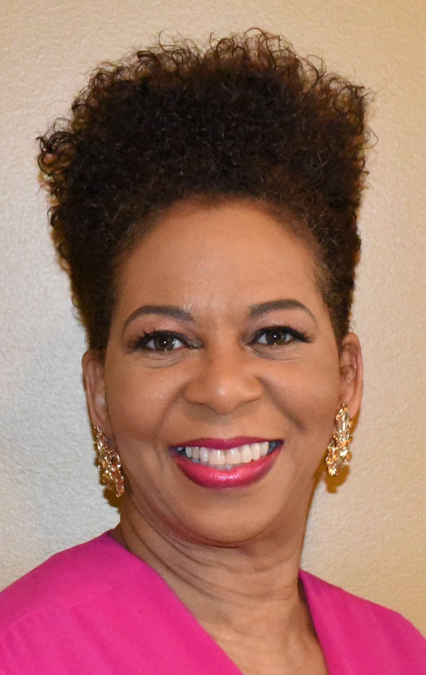 A woman wearing a pink shirt and earrings is smiling for the camera.