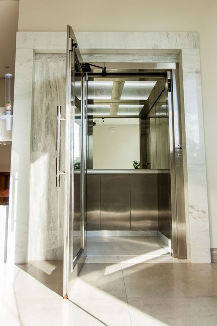 Moderna porta de elevador em aço inoxidável entreaberta em uma entrada com moldura de mármore.