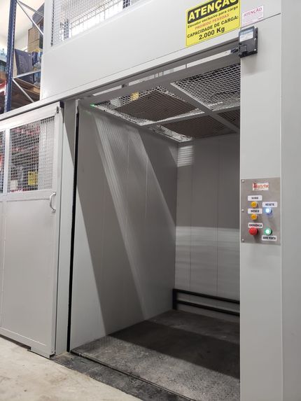 Elevador de carga industrial em um armazém com porta aberta e painel de controle, capacidade marcada como 2.000 kg.