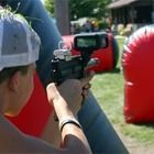 Person aiming a marker gun at an outdoor target course with red inflatable barriers