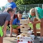 People playing giant Jenga outdoors by a pool, leaning in to pull wooden blocks.