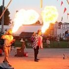 Fire performers in a street plaza, shooting bright flames into the air at dusk.