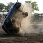 Blue car flipping onto its side in a dirt field, kicking up a large cloud of dust.