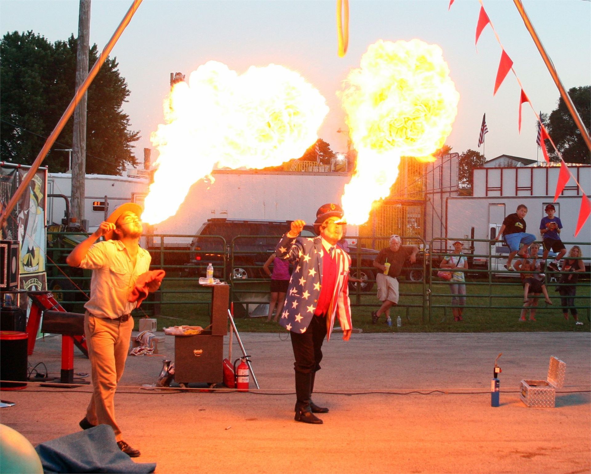 Two fire performers on stage with large flames shooting behind them at an outdoor show