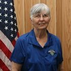 Woman in blue polo standing in front of an American flag and wood-paneled wall