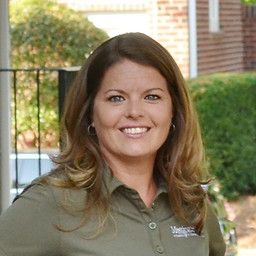 Woman with brown hair, smiling, wearing a green shirt, in front of a building.