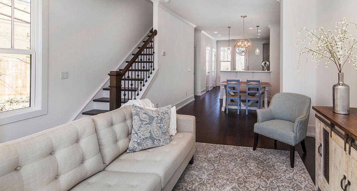 Living room with staircase, sofa, armchair, and dining area visible through an opening.