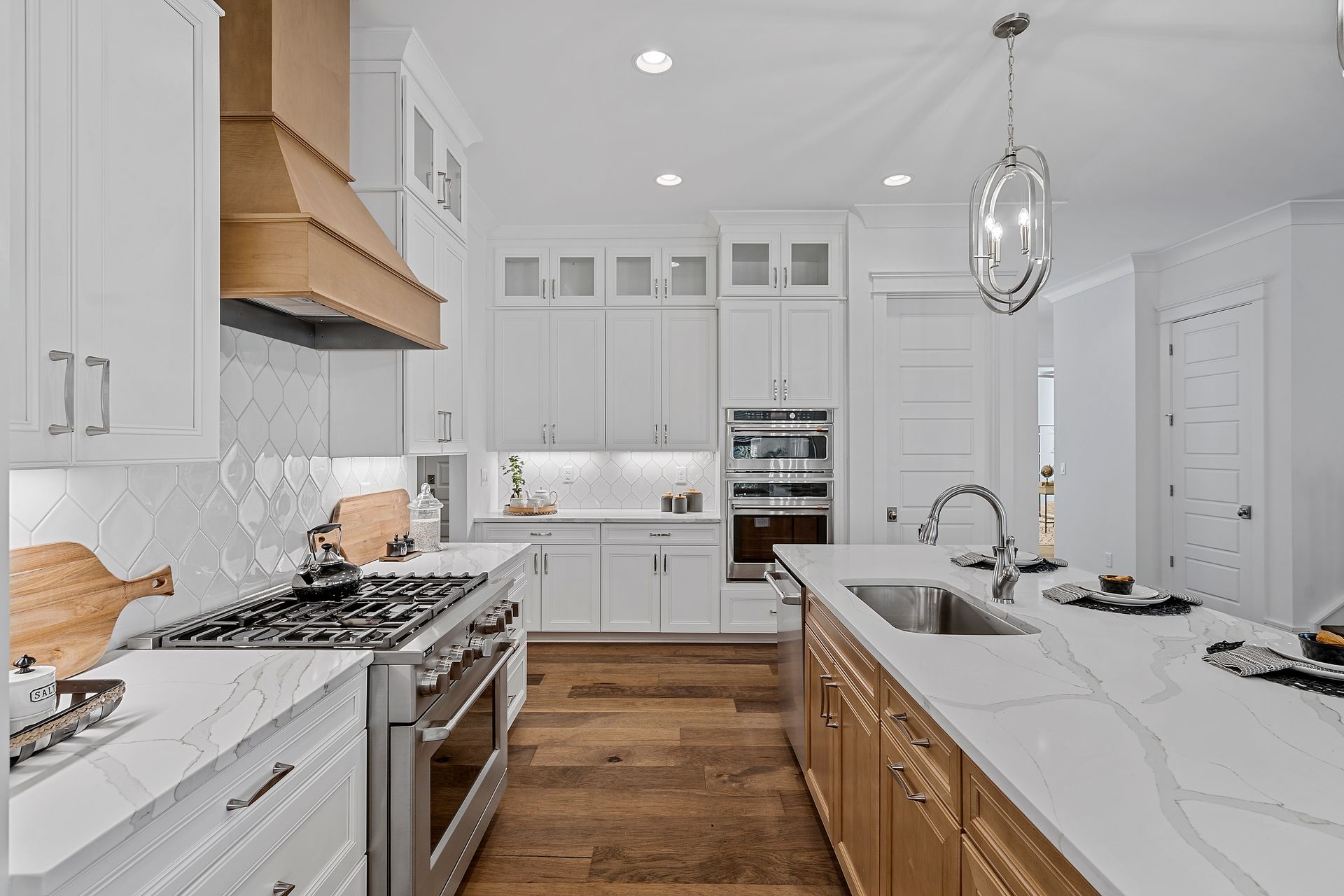 White kitchen with marble countertops, wood accents, and stainless steel appliances.